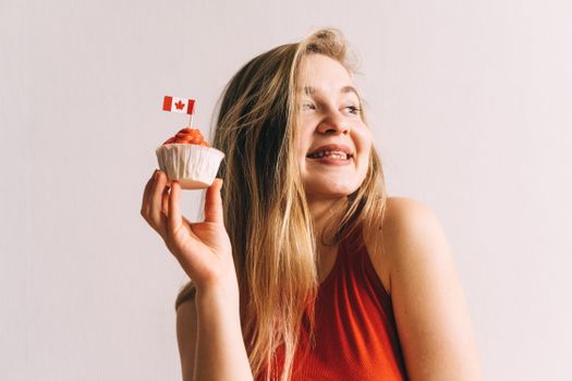 A happy woman in red holding a cupcake with a Canadian flag toothpick against a white background.