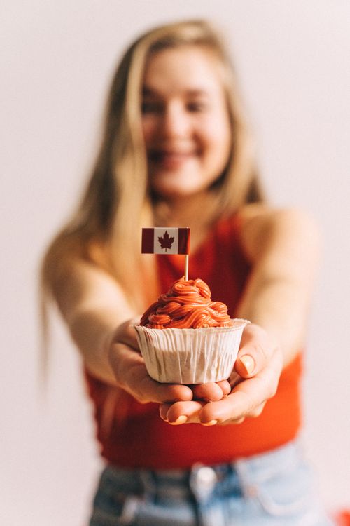 Free A smiling woman presents a cupcake with a Canadian flag against a blurred background. Stock Photo