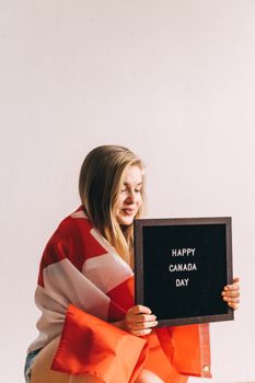 A woman wrapped in a Canadian flag holds a letter board reading 'Happy Canada Day.'