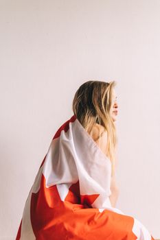 Young woman with blond hair wrapped in Canadian flag indoors, side pose.