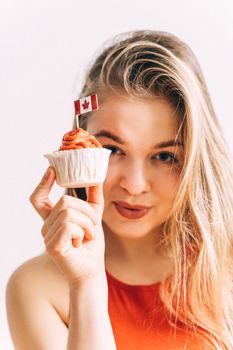 A young woman holding a cupcake with a Canadian flag and smiling joyfully.