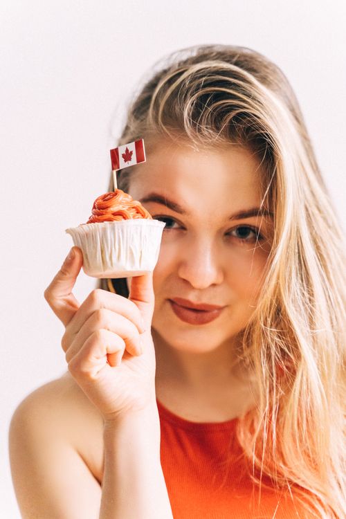 Free A young woman holding a cupcake with a Canadian flag and smiling joyfully. Stock Photo