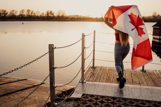 A woman with a Canadian flag walks on a dock at sunset, celebrating Canada Day in Toronto.