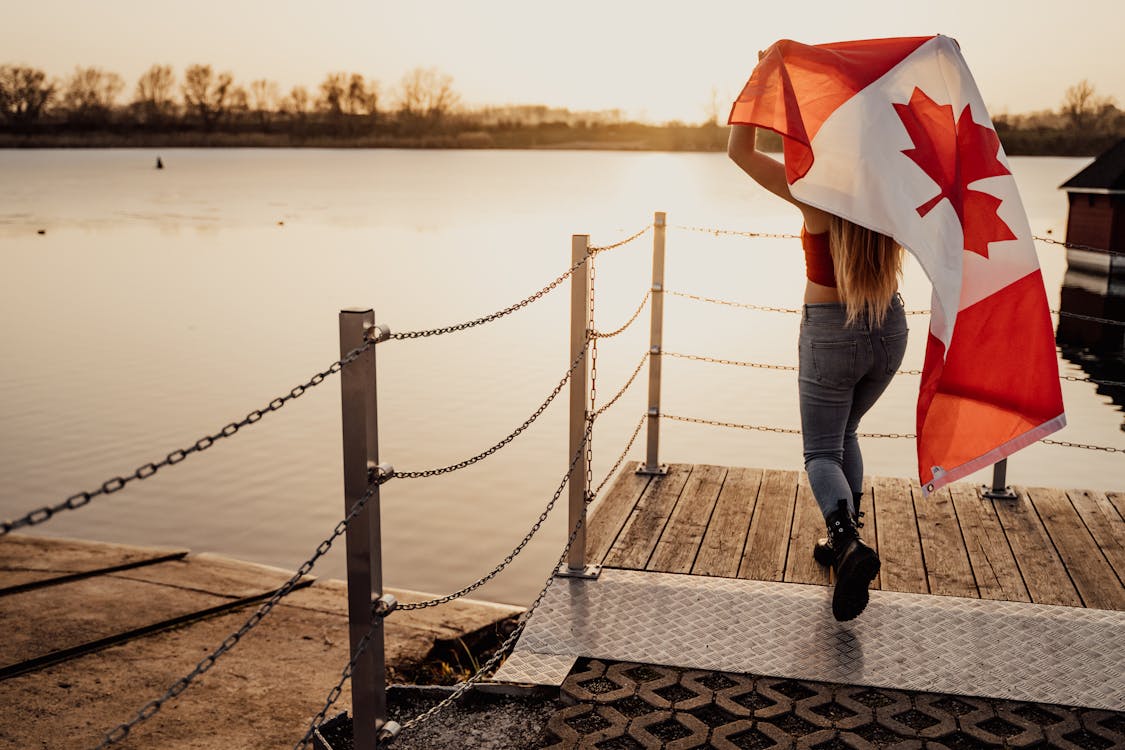 Back View Shot of a Woman Running while Holding a Canadian Flag