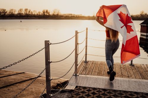 Free A woman with a Canadian flag walks on a dock at sunset, celebrating Canada Day in Toronto. Stock Photo