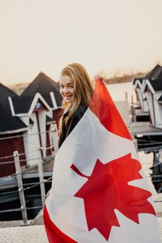 A woman joyfully holding a Canadian flag at sunset by a lakeside in Toronto.