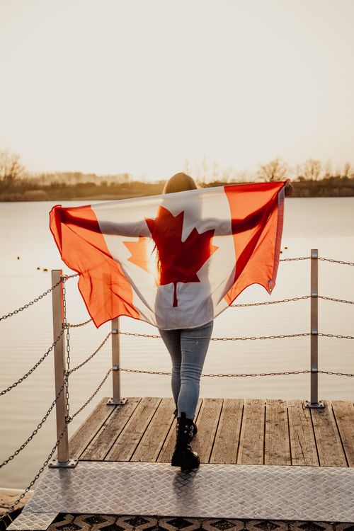 Free A person holding a Canadian flag by a lakeside in Toronto at sunset. Stock Photo