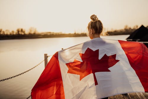 Back View Shot of a Woman Holding a Canadian Flag During Sunset