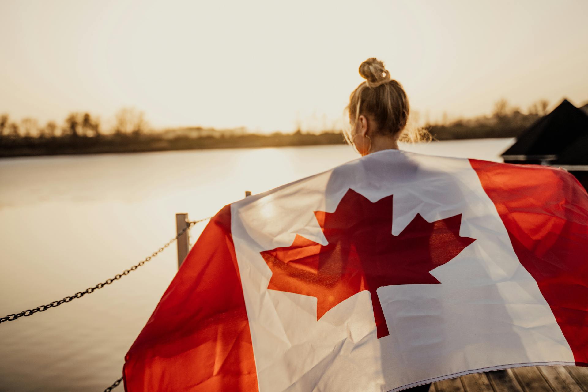 Back View Shot of a Woman Holding a Canadian Flag During Sunset
