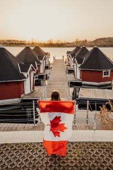 A woman wrapped in a Canadian flag stands on a lakeside dock at sunset near Toronto.
