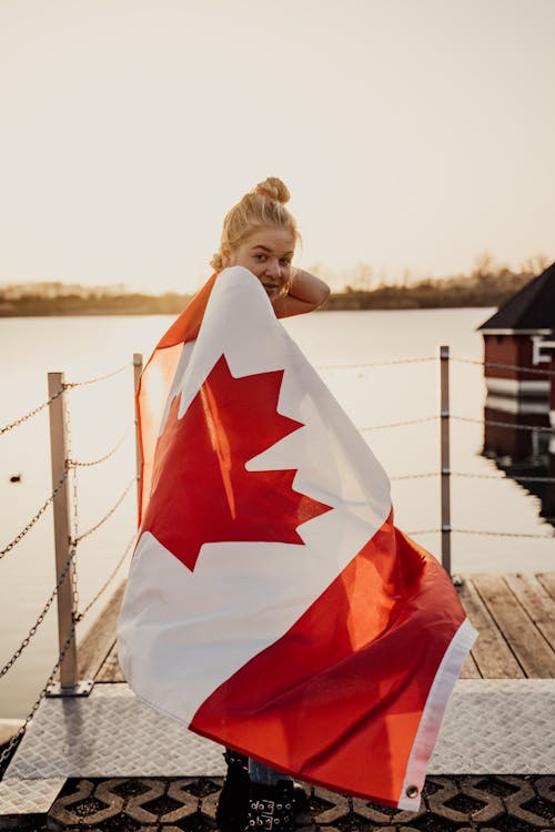 A Woman Holding a Canadian Flag Standing on a Wooden Dock while Smiling at the Camera