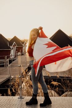 A young woman proudly holds the Canadian flag outdoors during a warm sunset in Toronto.