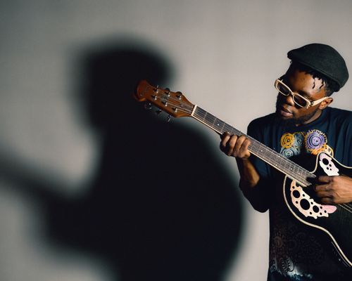 Free An African American man passionately playing an acoustic guitar, casting a dramatic shadow. Stock Photo