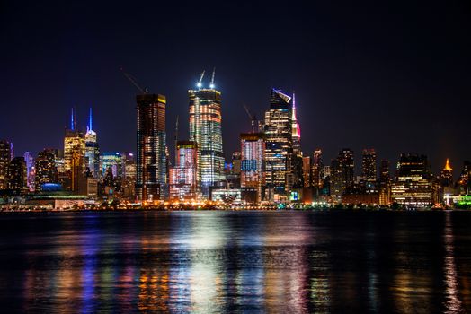 Vibrant nighttime view of the New York City skyline with skyscrapers reflecting on the river.