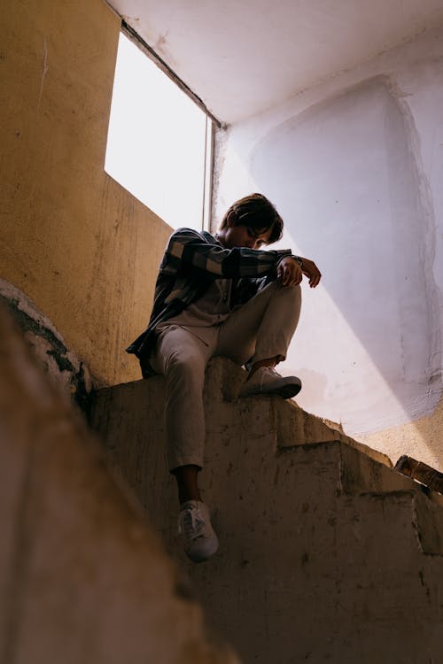 Free A Man in Plaid Long Sleeves Sitting on a Concrete Stairs of an Abandoned Place Stock Photo