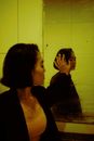 Side view of young depressed ethnic female in jacket reflecting in mirror with water drops while looking away indoors