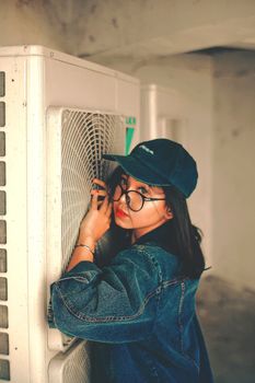 Side view of ethnic teenager in denim jacket and cap looking at camera while touching rack of air conditioning split system
