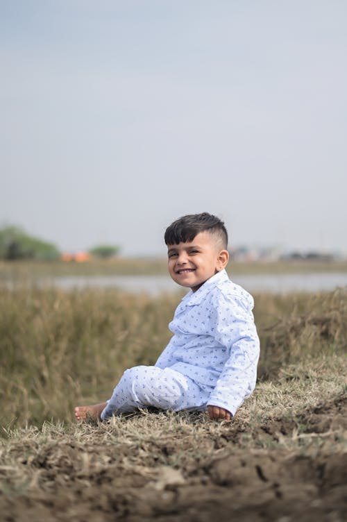 A Cute Little Boy Sitting on a Brown Field while Smiling at the Camera