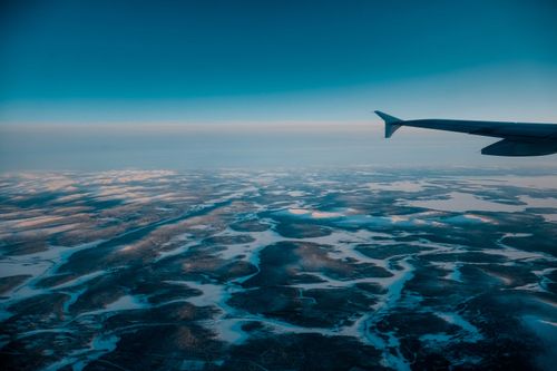 Free Wing of airplane flying in blue cloudless sky with skyline above vast terrain covered with snow in nature on winter day Stock Photo