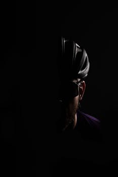 A silhouette of a cyclist wearing a helmet, captured in low light for a mysterious effect.