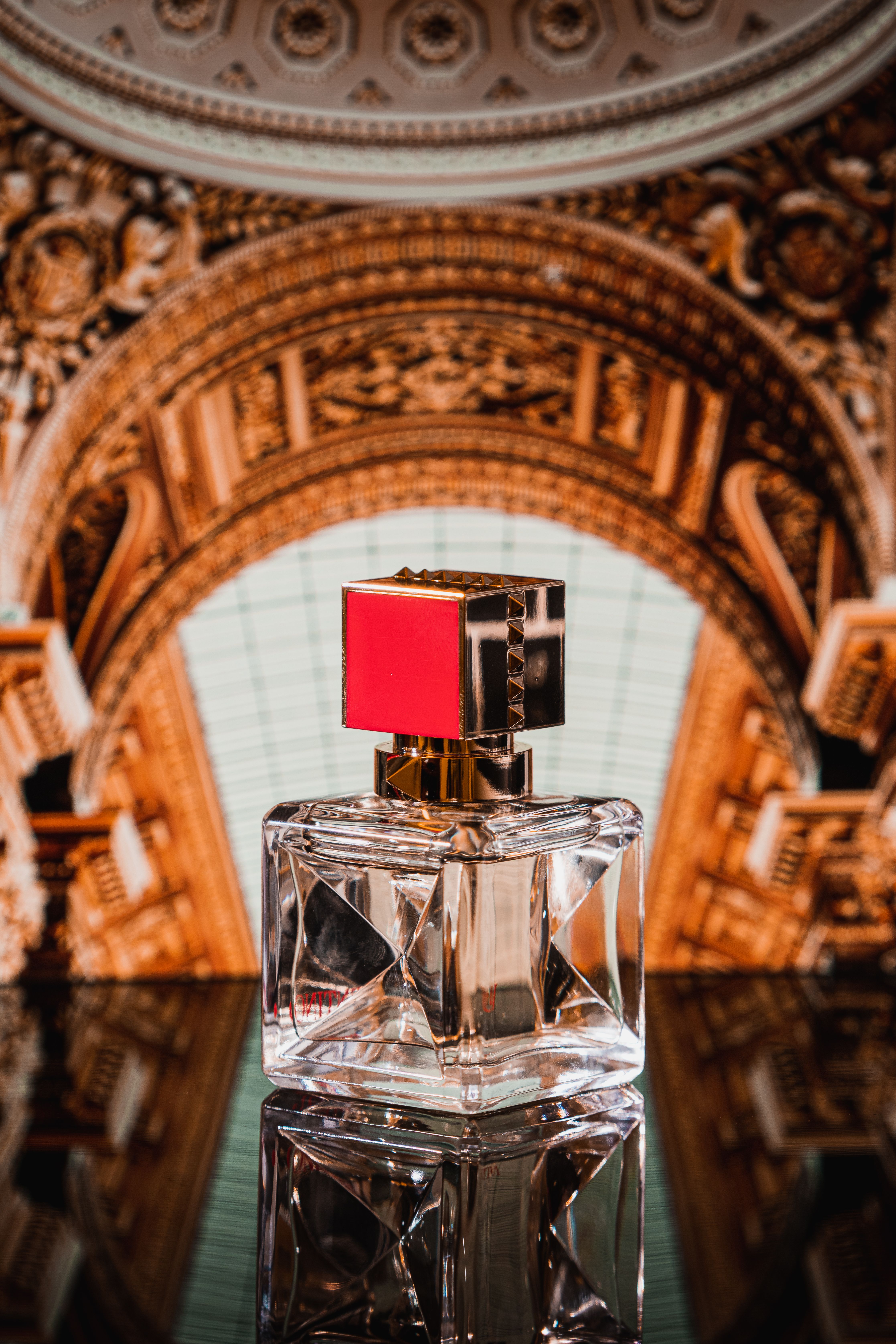 Luxurious men's cologne bottle on a reflective glass surface with ornate backdrop