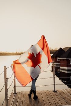 A person displaying a Canadian flag near the water at sunset in Toronto. Vibrant and patriotic.