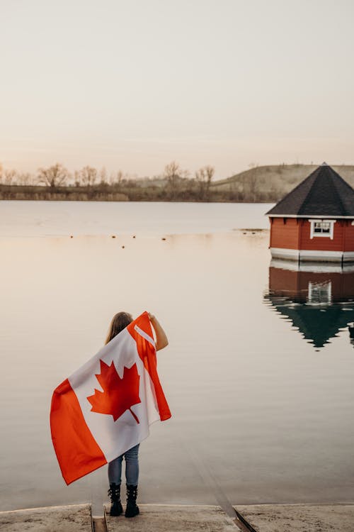 Free A Woman Holding a Flag while Facing a Lake Stock Photo