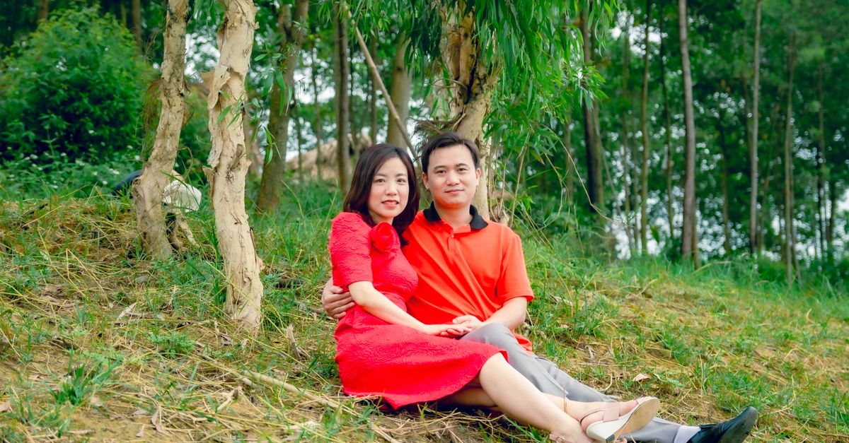 Asian couple enjoying a peaceful moment together on a grassy hill surrounded by trees.