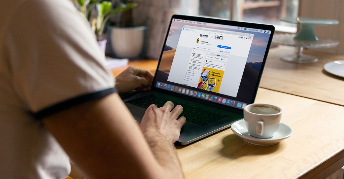 Casual home office setup with a person browsing the internet on a laptop next to a cup of coffee.