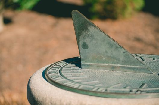Close-up of a vintage sundial in a garden setting, displaying Roman numerals.