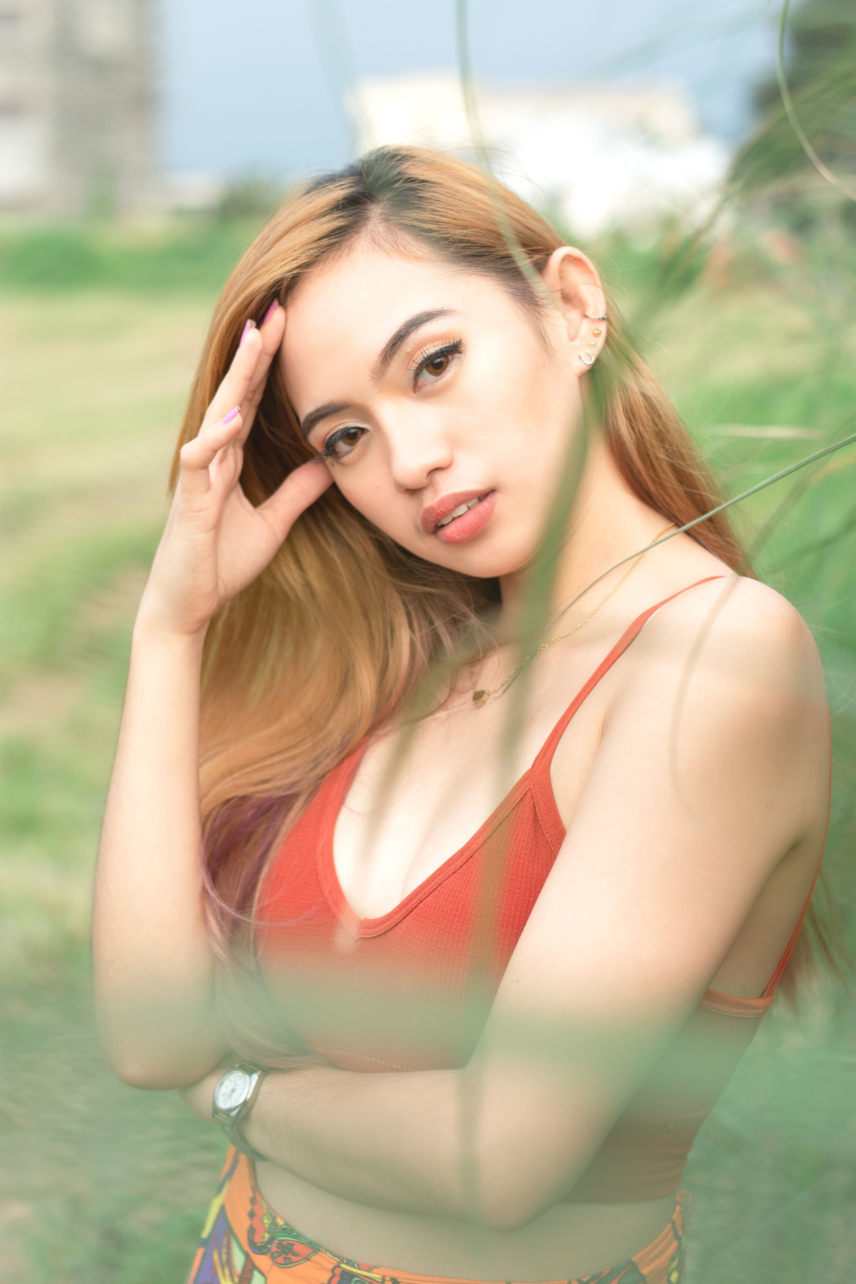 A beautiful woman in a red top poses outdoors with a serene expression.