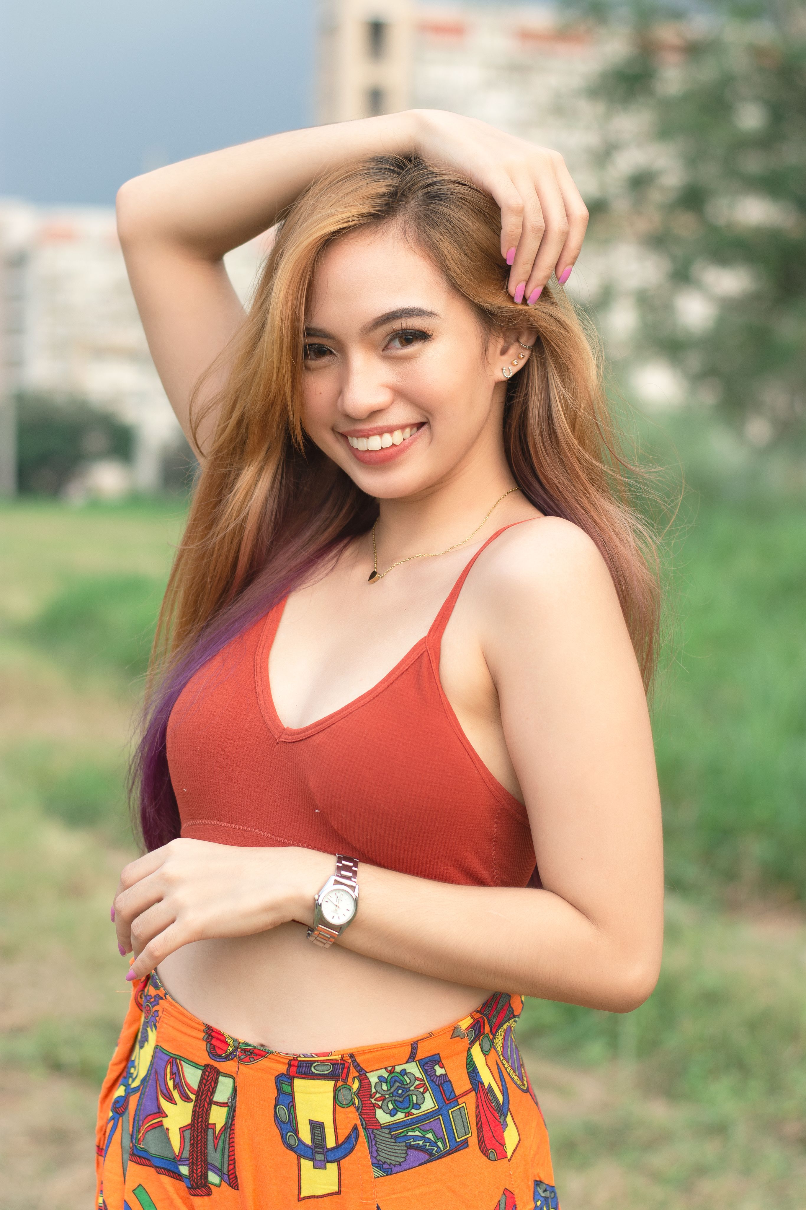 A young woman smiling in a red top, posing outdoors with a vibrant summer style.