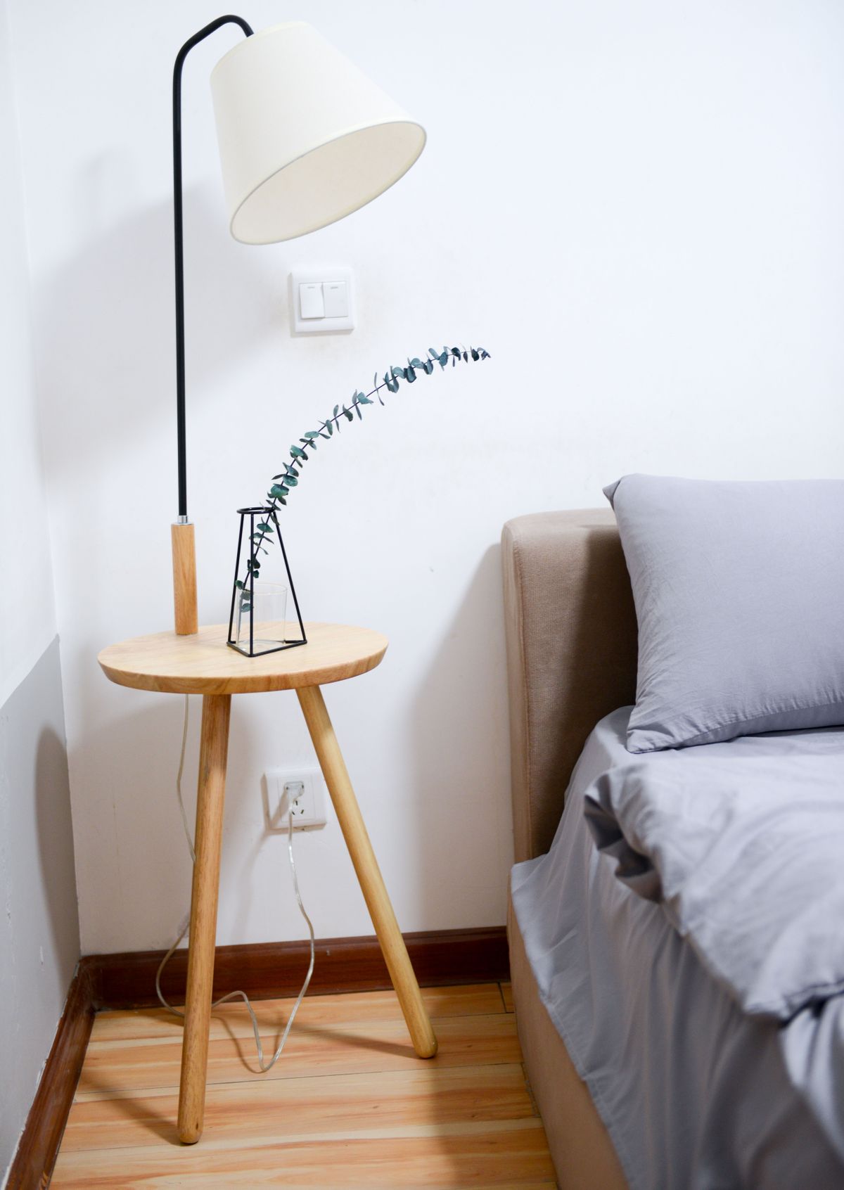 A warm white table lamp glowing softly on a nightstand beside a bed