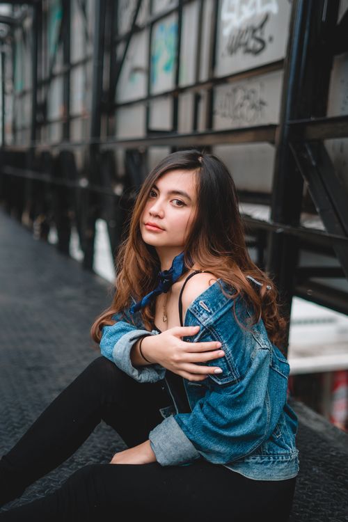 Free Fashionable young woman in a denim jacket posing outdoors with urban graffiti background. Stock Photo