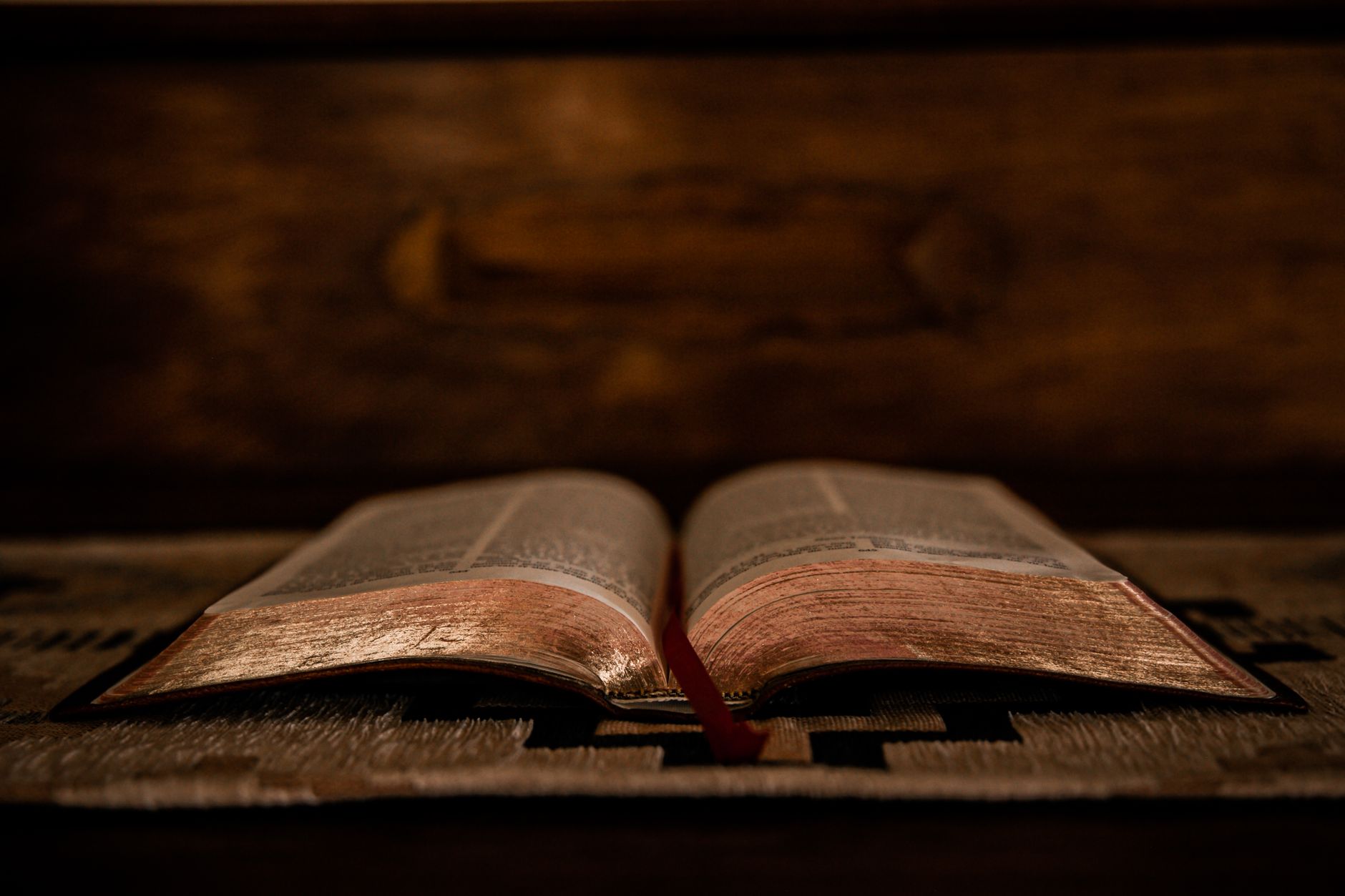 A dimly lit open Bible displayed on a wooden altar, highlighting its pages.