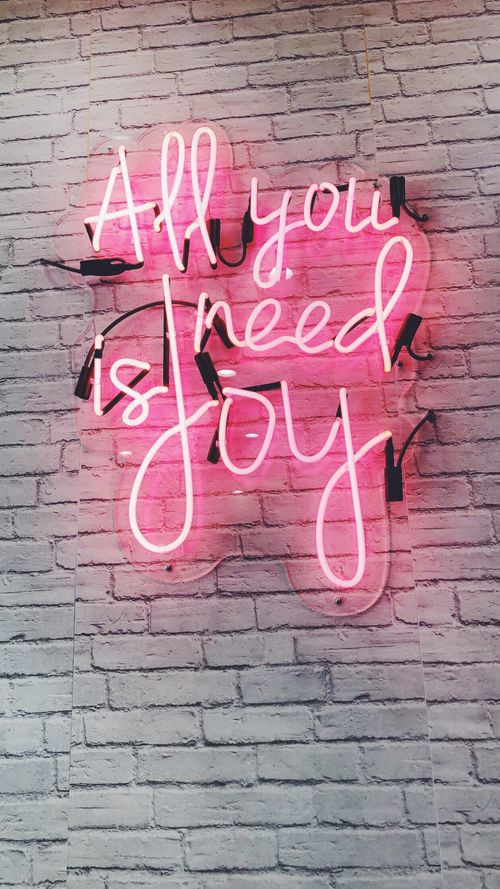 Free Bright pink neon sign with 'All You Need is Joy' text on a brick wall. Stock Photo