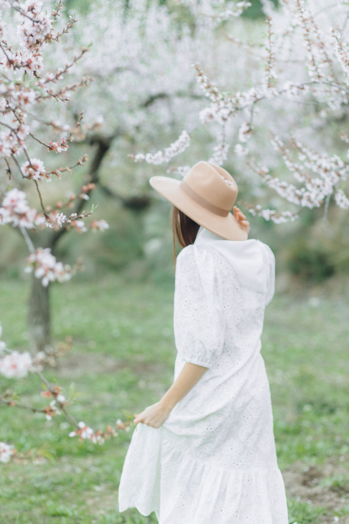 Back view of a woman in a white dress and brown hat — the timeless ease of broderie