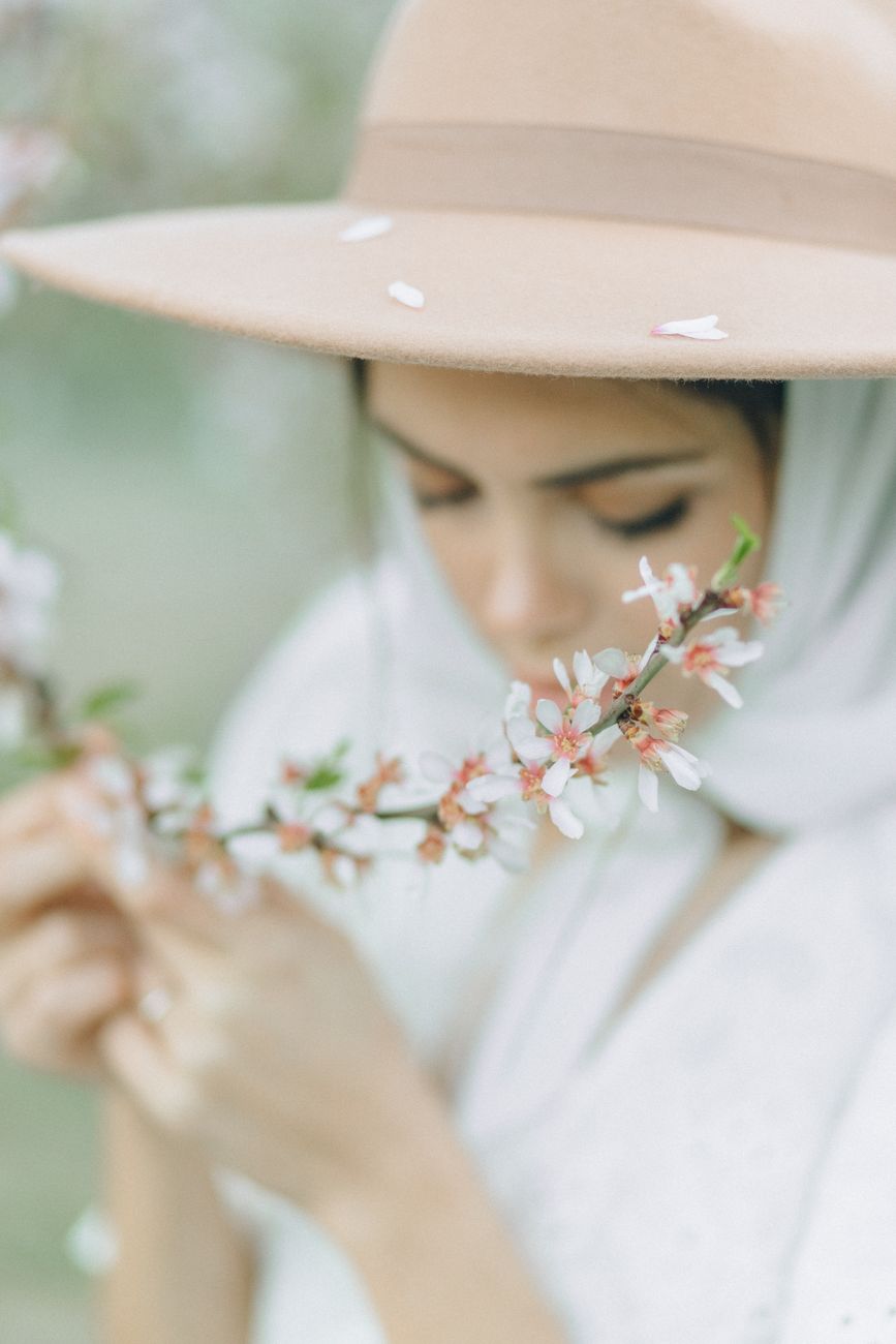 A woman in a hat admires delicate spring cherry blossoms in soft focus.