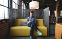 年轻人坐在现代共享办公空间的沙发上，用笔记本写作