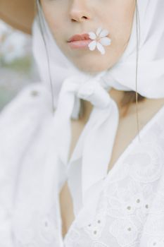 Closeup of a woman's lips adorned with a small white flower, wearing a headscarf.
