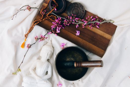 A serene Buddhist meditation setup featuring a white Buddha figurine, pink flowers, and a Tibetan singing bowl.