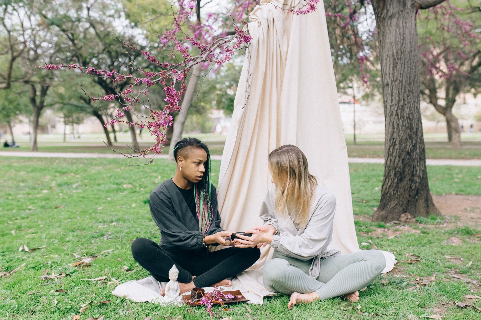 Two women engage in a peaceful meditation session outdoors under blossoming trees, promoting tranquility and connection.
