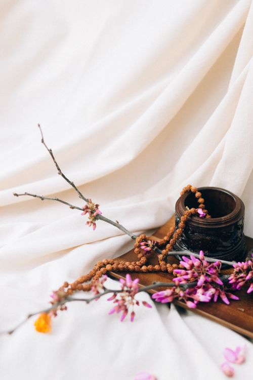 Free A beautiful floral arrangement with purple flowers, wooden vase, and beads on a white fabric background. Stock Photo