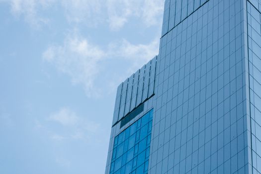 Low angle of contemporary skyscrapers with glass mirrored facades against cloudy blue sky on sunny day