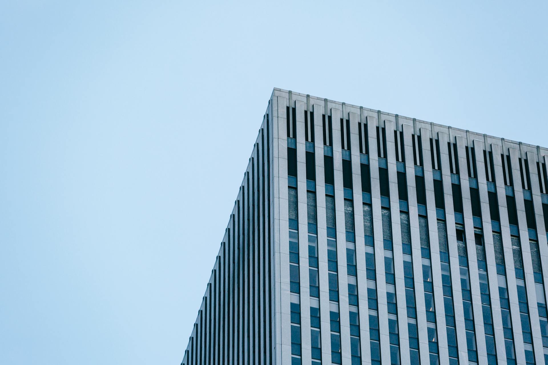 From below of geometric facade and corner of contemporary multistory commercial building against cloudless blue sky