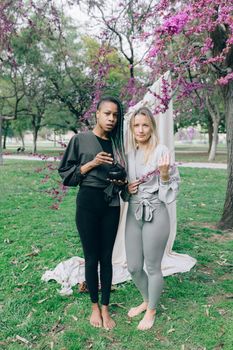 Two women standing in a park under blooming trees, radiating calm and joy.