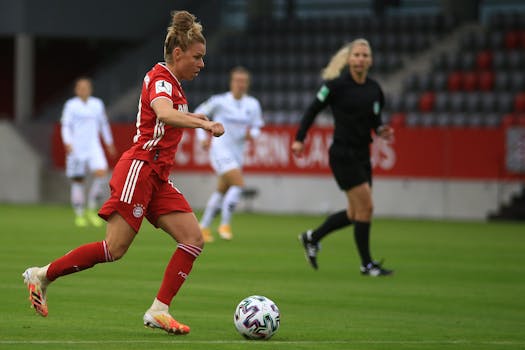 A female soccer player in red uniform dribbles during a match.