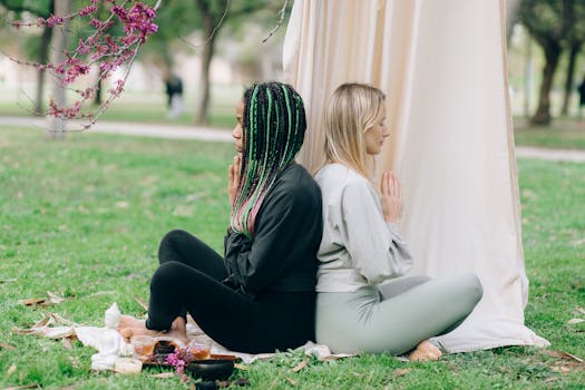 Two women meditating back-to-back in a serene outdoor setting, promoting wellness and relaxation.