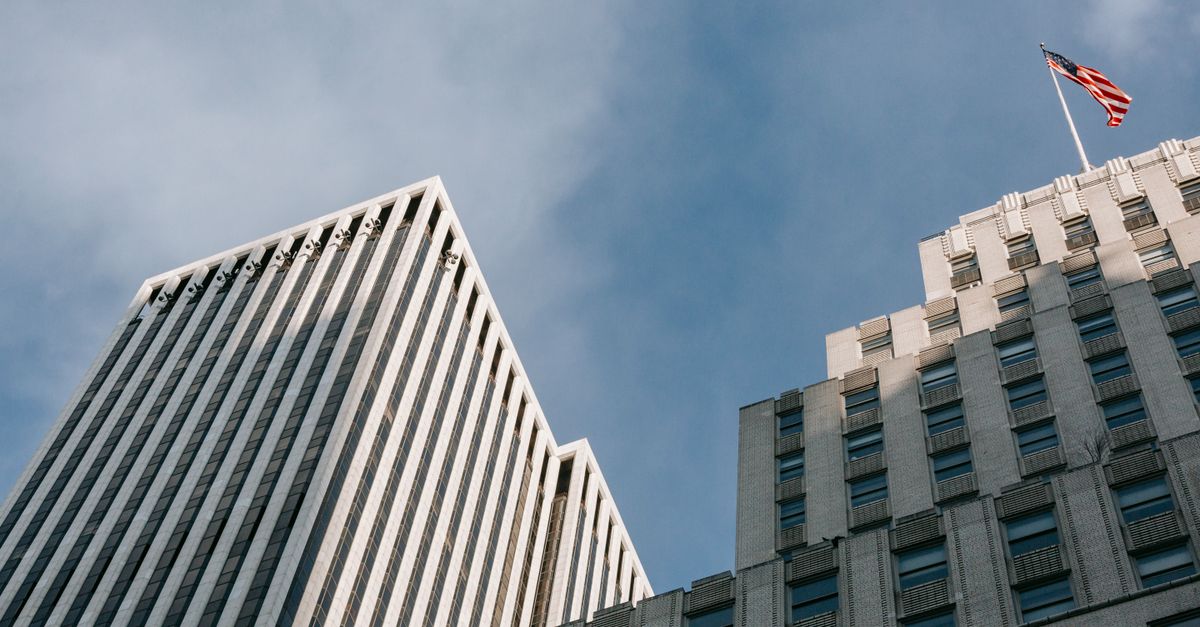 Low angle of high multistory office skyscrapers with waving American flag located in downtown of megalopolis
