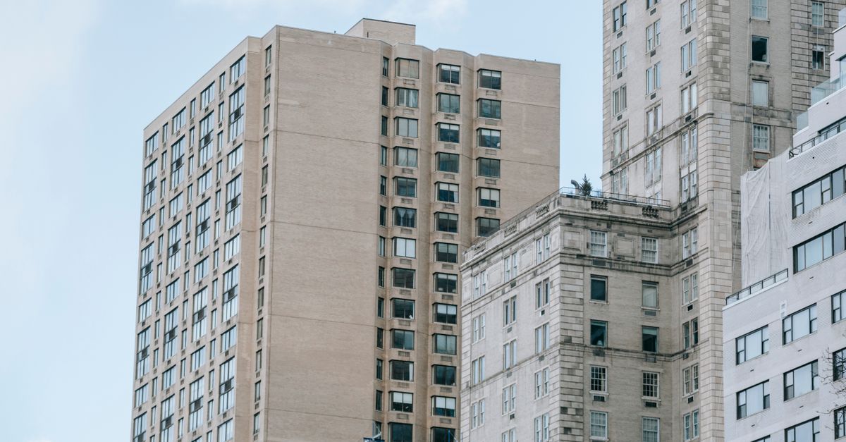 Low angle of tall multistory apartment buildings with balconies located in residential district against blue sky